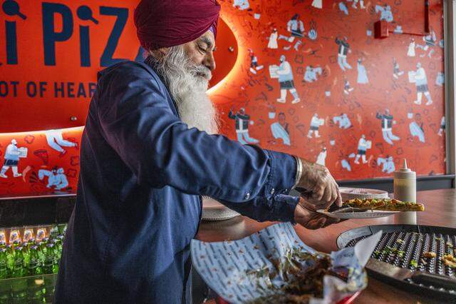 Paul Singh, the father of one of the owners of Tandoori Pizza at Downtown Commons, serves pizza on Oct. 15, 2025, to guests during the restaurant's grand opening.